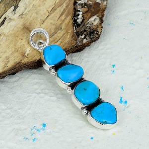 May include: A silver pendant featuring four vertically aligned, smooth, bright blue turquoise stones set in polished metal. The pendant includes a circular bail at the top for attachment, showcasing a linear design with rounded, organic stone shapes.