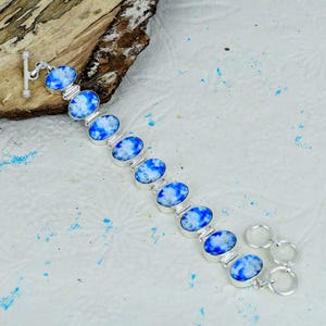 Può includere: Un bracciale a maglie in argento con nove pietre ovali caratterizzate da un motivo marmorizzato blu brillante e bianco. Il bracciale è dotato di una chiusura a barra a un'estremità e di due anelli circolari aggiuntivi per la regolazione.