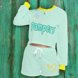 May include: A mint green two-piece pajama set with long sleeves and shorts. The top has a yellow trim and the text "Pamper" in green. The shorts have a yellow heart design.