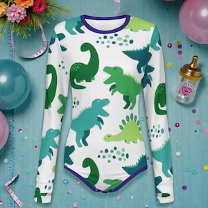 May include: White long-sleeved baby bodysuit with a pattern of green and teal dinosaurs. The bodysuit has a purple trim around the neckline and legs. The background is a light blue surface with balloons and confetti.