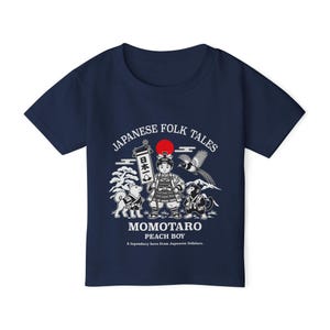 Pode incluir: Uma t-shirt azul-marinho de manga curta com uma estampa gráfica branca de Momotaro, um cão, um macaco e um faisão. O texto diz JAPANESE FOLK TALES, MOMOTARO PEACH BOY, A legendary hero from Japanese folklore e caracteres japoneses.