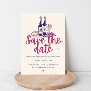 May include: Save the date card with a wine and cheese theme. The card features a hand-drawn illustration of wine bottles, glasses, cheese, and grapes. The text on the card reads "Save the date" in a pink script font. The date and time of the event are listed below the illustration, along with the address and RSVP information.