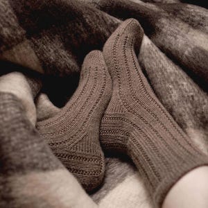 May include: A pair of brown knitted socks with a textured pattern, resting on a brown and white checked blanket.