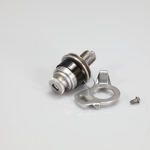 May include: A metallic cylindrical component with a knurled top, a black central band, and a threaded base. It is accompanied by a flat, silver-colored metal bracket with a circular cutout and a small, separate threaded screw.