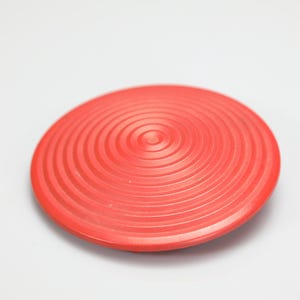 Könnte beinhalten: Ein kreisförmiges rotes Balance-Pad mit einer strukturierten Oberfläche aus konzentrischen Ringen, die von der Mitte ausgehen. Das kuppelförmige Fitnessgerät hat ein glattes, abgerundetes Profil und eine feste Struktur für Stabilitätsübungen.