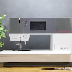 Op de afbeelding: Een witte en grijze Pfaff naaimachine met een digitaal display en rode knoppen. De machine heeft de tekst "Pfaff" op de voorkant en "quilt ambition 630" op de zijkant. Een schaar en spoelen garen staan op de voorgrond.