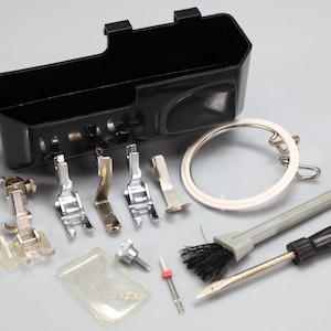 Può includere: Un kit di accessori per macchina da cucire con un contenitore in plastica nera, sei piedini in metallo e plastica trasparente, una guida metallica circolare, un piccolo cacciavite, una spazzolina, un ago e una vite metallica.