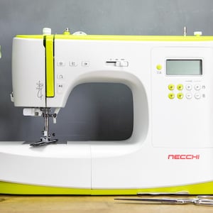 Op de afbeelding: Een witte en gele Necchi naaimachine met een digitaal display en bedieningsknoppen. De machine heeft een gebogen arm en een naald, met een schaar en spoelen garen in de buurt. De machine staat op een houten oppervlak.