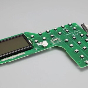 May include: A green printed circuit board featuring a rectangular black LCD screen on the left side and a grid of small square buttons on the right. The board is labelled JANOME 846-K and includes a white ribbon cable connector at the top right edge.