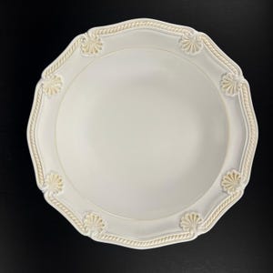 May include: A round, off-white ceramic bowl featuring a scalloped edge with a raised rope-like texture and decorative shell-shaped motifs at regular intervals along the rim. The center of the bowl is smooth, plain, and concave in shape.