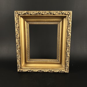 May include: A rectangular picture frame with a metallic gold finish. The frame features an ornate, raised leaf-like pattern along the outer edge and a smaller, beaded texture bordering the inner opening, creating a layered, dimensional appearance.