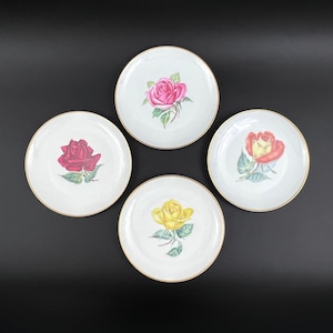 May include: Set of four white ceramic plates with gold trim, each featuring a different coloured rose with green leaves. The roses are pink, red, yellow, and orange.