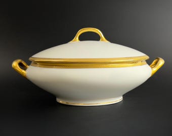 May include: White porcelain serving dish with a gold rim and handles. The dish has a lid with a gold handle.
