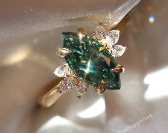 May include: A gold ring featuring a central marquise-cut dark green gemstone surrounded by smaller, clear, pear-shaped stones. The setting is metallic gold, and the text SaintSapphires is visible in multiple locations on the surrounding fabric.