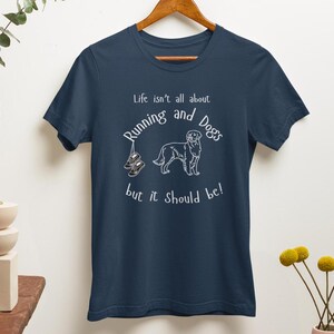 以下が含まれることがあります： 白のテキストとグラフィックが特徴のネイビーブルーのTシャツ。「Life isn't all about Running and Dogs but it should be!」というテキストと犬のイラスト、ランニングシューズが描かれています。