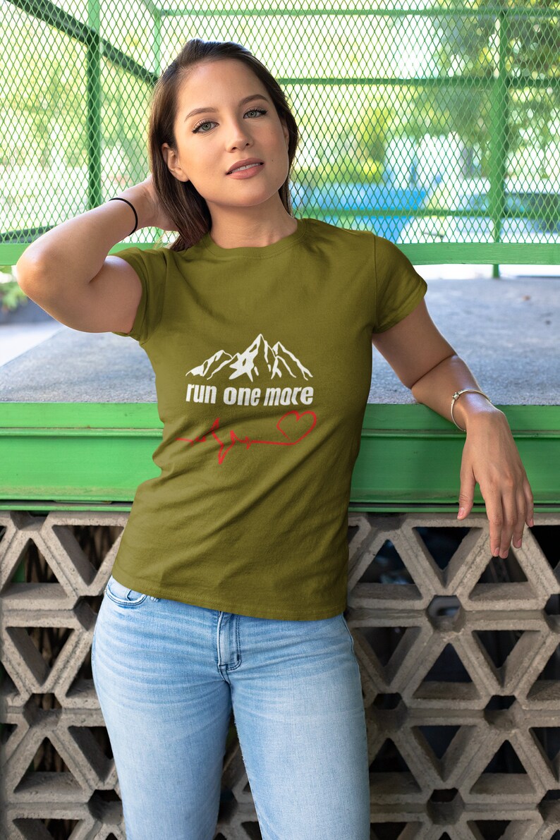 May include: A woman wearing a green t-shirt with a white mountain graphic and the text "run one more" with a red heart beat line.