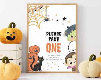 May include: A framed Halloween print with the text "PLEASE TAKE ONE". The print features cartoon pumpkins, a black cat, a spider web, ghosts, and other Halloween characters. Decorative plush pumpkins are in the foreground. The print is in a wooden frame.