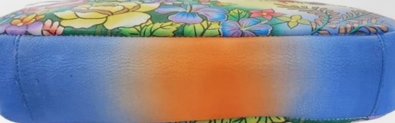 May include: A blue leather handbag with a floral print and a gradient ombre effect on the bottom. The bottom of the bag is a light blue color that fades to orange.