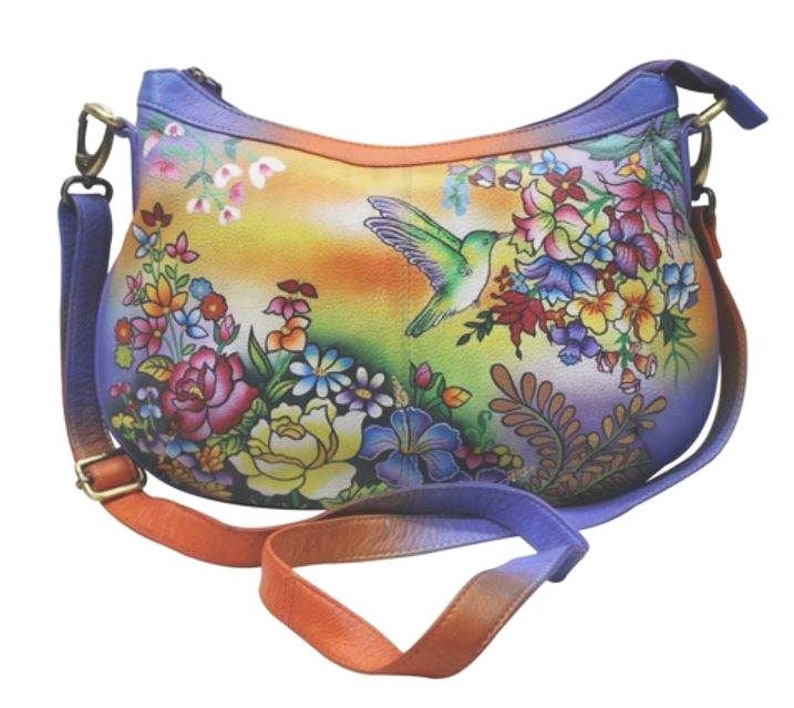 May include: A colorful leather handbag with a floral and hummingbird design. The bag has a long adjustable strap and a top zipper closure.