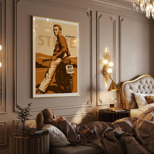 May include: A framed poster featuring Steve McQueen on a motorcycle, with a sepia-toned color scheme. The poster has the word "STEVE" in large letters and "McQueen" at the top. The motorcycle's license plate reads "WP 13371".