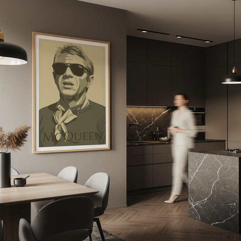 May include: A framed art print featuring a stylized portrait of Steve McQueen wearing sunglasses. The print has a neutral color palette with the word "McQueen" at the bottom. The artwork hangs on a wall in a modern kitchen setting.