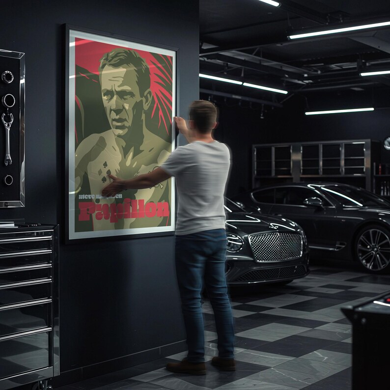 May include: A framed poster with a man's image and red and green tones is being hung on a dark wall. The poster has the text "nice to see you, Pavillon". A person is hanging the poster in a garage with a car.