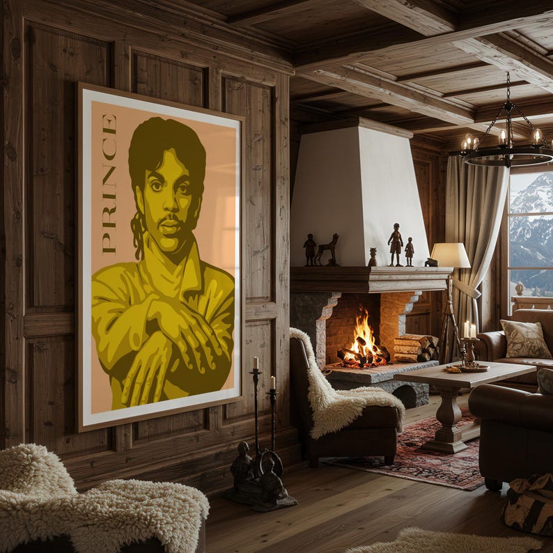 Op de afbeelding: Een ingelijste poster met een gestileerde afbeelding van Prince in gele en bruine tinten. Het woord "PRINCE" staat verticaal afgedrukt. Het kunstwerk hangt aan een houten wand in een gezellige woonkamer met een open haard.