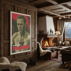 May include: A framed poster with a portrait of a man with tattoos, set against a red and green backdrop. The poster reads "Steve McQueen Papillon". The room has wooden panelling and a fireplace with a burning fire.