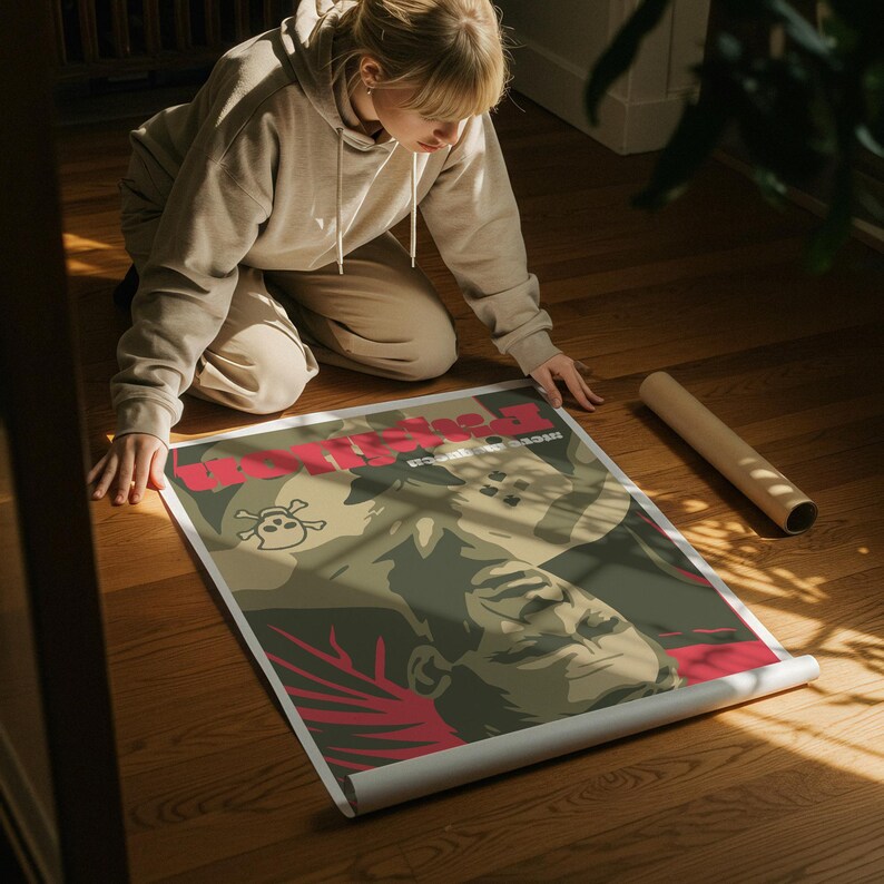 May include: A poster with a stylized illustration in red, green, and tan tones. The poster has red text and a skull and crossbones graphic. The poster is unrolled on a wooden floor.