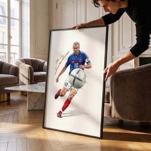 Pode incluir: Obra de arte emoldurada com uma ilustração dinâmica de um jogador de futebol com uma camisa azul com o número 10, chutando uma bola de futebol. A obra inclui uma assinatura e está em um fundo branco dentro de uma moldura preta.