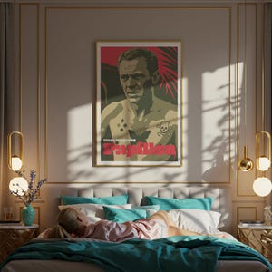 May include: A framed poster featuring a stylized image of a man with tattoos, including a butterfly and skull. The poster has the word "Papillon" in red. The poster is hanging above a bed with teal and white pillows and a teal blanket. A person is lying on the bed.