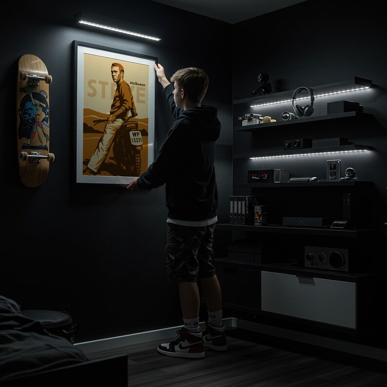 May include: A framed poster featuring Steve McQueen in a brown jacket and white pants, with the text "McQueen" and "STEVE". A skateboard hangs on the wall to the left. The room is dark with built-in shelves and LED lighting.