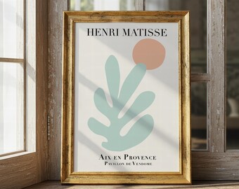 May include: A framed art print featuring a minimalist design by Henri Matisse. The artwork includes a light green leaf shape, a peach-colored circle, and text that reads "AIX EN PROVENCE PAVILLON DE VENDOME". The frame is gold-colored.
