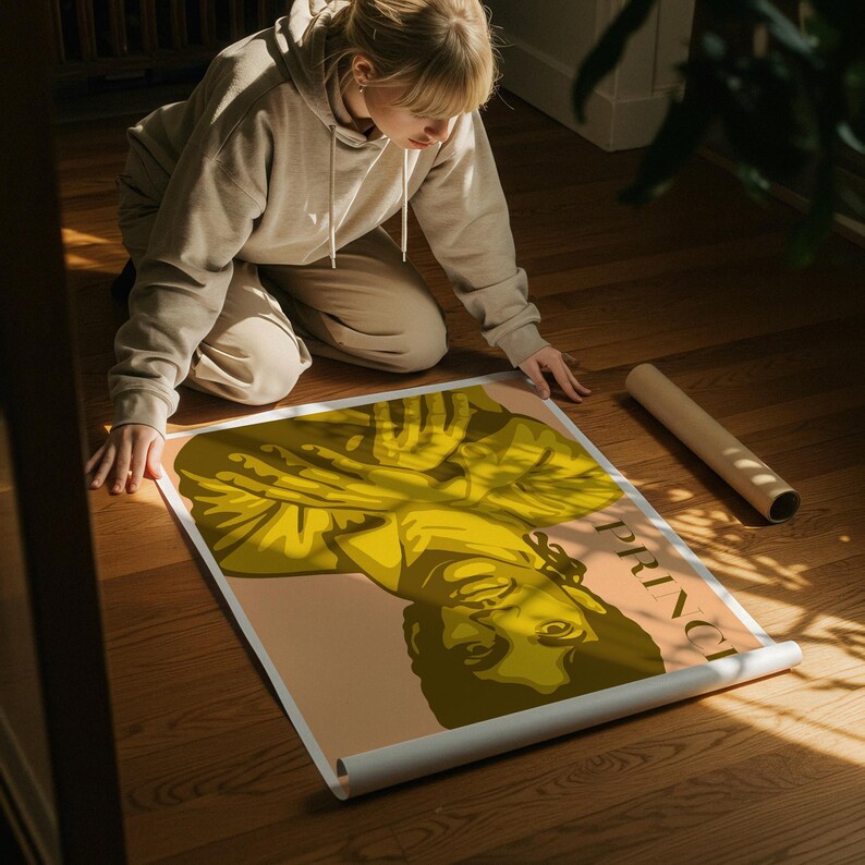 Op de afbeelding: Een poster met een gestileerde illustratie van Prince in tinten geel en bruin. Het woord "PRINCE" staat verticaal aan de rechterkant gedrukt. De poster is gedeeltelijk uitgerold op een houten vloer.