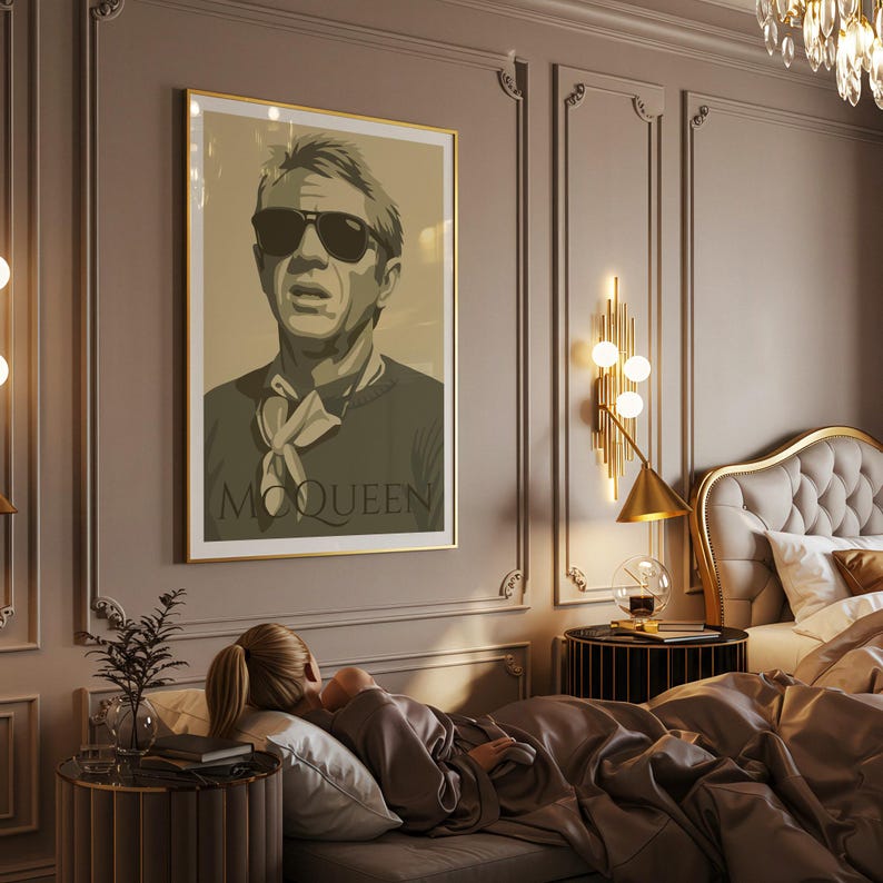 May include: A framed poster featuring a stylized portrait of Steve McQueen wearing sunglasses. The poster has a gold frame and the word "McQueen" is printed at the bottom. The image is displayed in a bedroom setting.