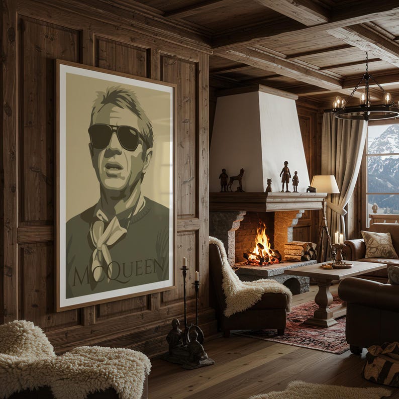 May include: A framed poster featuring a stylized portrait of a man wearing sunglasses, a sweater, and a scarf, with the name "McQueen" printed below. The poster hangs on a wood-paneled wall in a cozy, rustic living room setting.