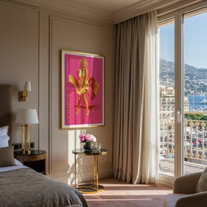 Puede incluir: Un p&oacute;ster enmarcado con Marilyn Monroe con un vestido dorado sobre un fondo rosa, con el nombre "MONROE" impreso verticalmente. La habitaci&oacute;n tiene una cama, una mesita de noche con una l&aacute;mpara y una mesa peque&ntilde;a con flores y un vaso. Una gran ventana ofrece vistas a una ciudad y al mar.