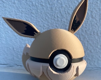 Può includere: Una Poké Ball a tema Eevee stampata in 3D, color beige e bianco. Presenta grandi orecchie a punta con dettagli marroni e neri, un bottone bianco e una fascia nera. Il design include una coda soffice e un aspetto strutturato dettagliato.