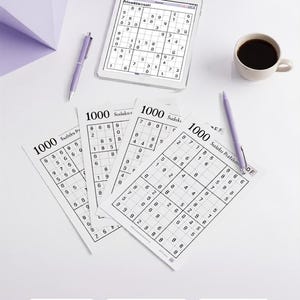 Könnte beinhalten: Eine Sammlung von 1000 Sudoku Puzzles mit gedruckten Blättern mit Zahlengittern, einem Tablet mit einem Puzzle, zwei lila Stiften und einer weißen Tasse mit schwarzem Kaffee. Der Text 1000 Sudoku Puzzles, Easy, Medium, Hard, Instant Download ist sichtbar.