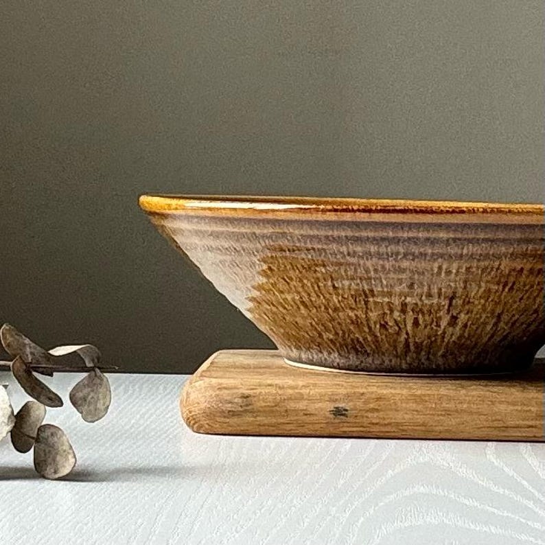 May include: A large, brown ceramic bowl with a wide, shallow shape and a slightly flared rim. The bowl has a textured, speckled glaze with a subtle sheen.
