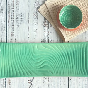 Op de afbeelding: Een rechthoekige serveerschaal van groen keramiek met een golvend, getextureerd ontwerp. De schaal is rechthoekig en heeft afgeronde randen.