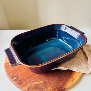 Könnte beinhalten: Eine tiefblaue und violette Keramik-Backform mit zwei Griffen. Die Form hat eine glänzende Oberfläche und steht auf einer Holzoberfläche.