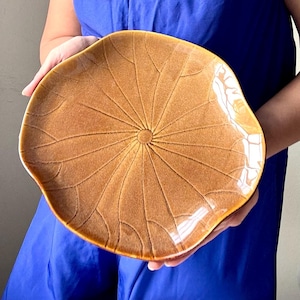 Może przedstawiać: Duży, brązowy ceramiczny talerz do serwowania z wzorem liścia lotosu. Talerz ma wypukłe centrum i lekko falisty brzeg.