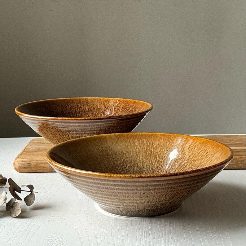May include: Two brown ceramic bowls with a textured glaze. The bowls are nested together, with the larger bowl on top of the smaller bowl.