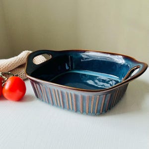 Könnte beinhalten: Eine blaue Keramik-Backform mit zwei Griffen. Die Form hat eine braune Glasur und ein geripptes Design.