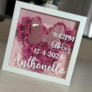 Puede incluir: Un marco blanco con un fondo rosa y un diseño floral. El diseño incluye formas de mariposas rosas brillantes y rosas de papel. El texto dice "9:42PM 6lb 8oz 17-4-2024 Anthonella".