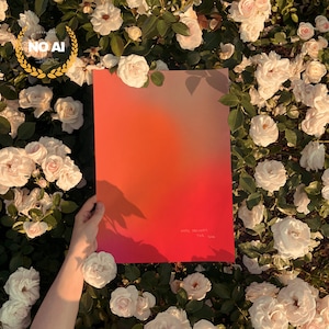 Puede incluir: Una vibrante impresión artística con un degradado de tonos naranja y rojo, sostenida contra un fondo de rosas blancas. La impresión presenta el texto "HOPE ALWAYS THE SUN". La obra de arte está rodeada de exuberante vegetación y flores.