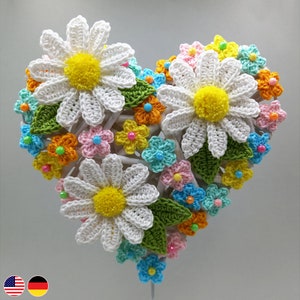 Könnte beinhalten: Ein gehäkelter Herz-Wandbehang mit weißen Gänseblümchen und bunten Blumen. Die Gänseblümchen haben gelbe Zentren und die anderen Blumen sind in Schattierungen von Rosa, Blau, Gelb und Orange.