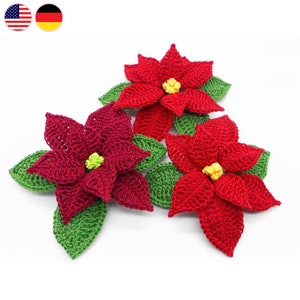 Può includere: Tre fiori di stella di Natale all'uncinetto con foglie verdi. I fiori sono rossi con centri gialli.