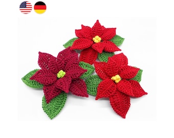 May include: Three crocheted poinsettia flowers with green leaves. The flowers are red with yellow centers.